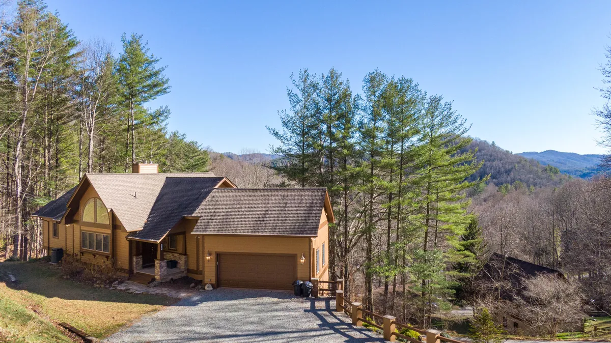This image shows the exterior of Moonlight Manor with its welcoming facade nestled among mature trees. The mountain view in the background hints at the proximity to outdoor adventures, while the driveway and porch suggest easy access after a day exploring nearby attractions.