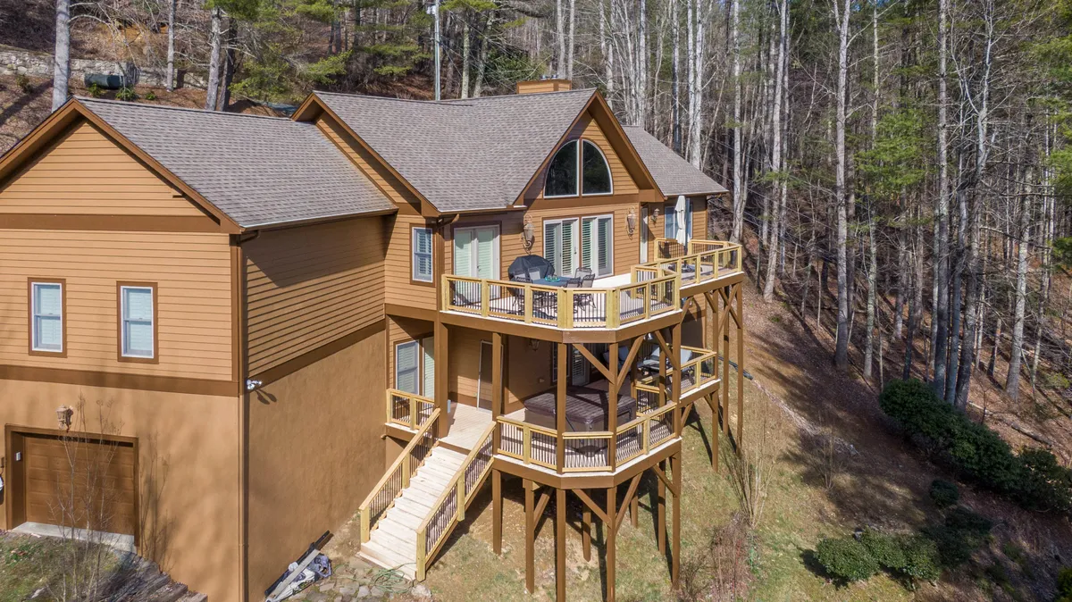 This image captures a wooden deck with large windows that provide a seamless transition between the indoor living spaces and the surrounding natural environment. The deck itself is designed for relaxation, offering a peaceful spot to enjoy the sunrise or sunset, with lush trees providing privacy and serenity.