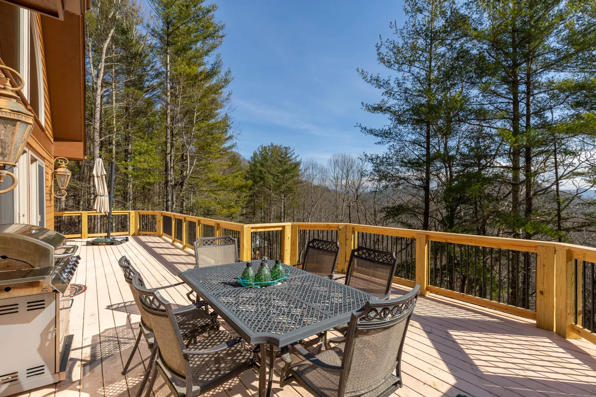 A scenic deck set with an outdoor dining table and grill, overlooking a backdrop of trees. The space is ideal for social gatherings or quiet moments taking in the mountain air, embodying the spirit of all-season enjoyment.