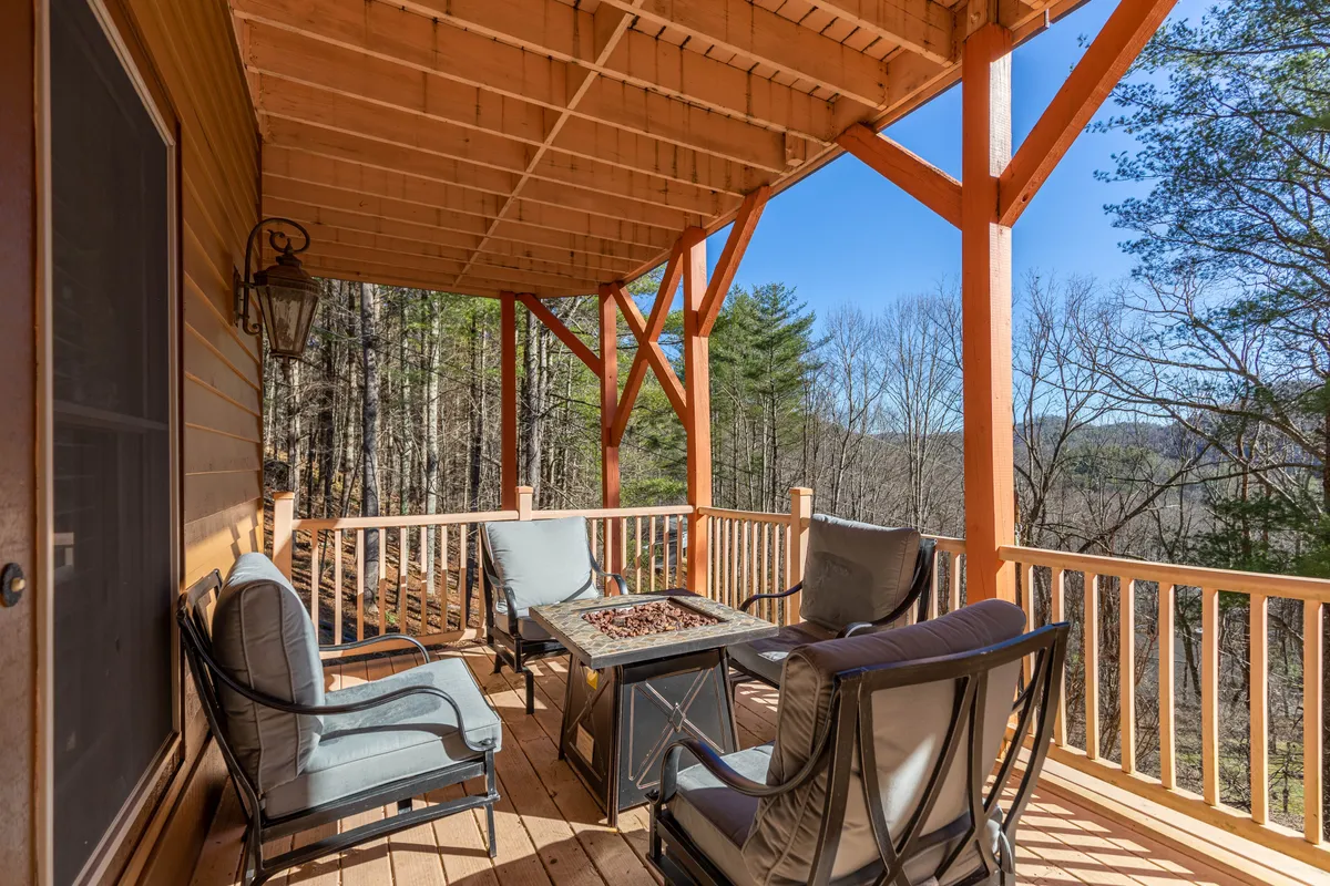 A stylish outdoor seating arrangement with a fire pit table sits on the deck, surrounded by the natural landscape. The setting is ideal for gathering with friends or family, sharing stories, or stargazing into the evening.