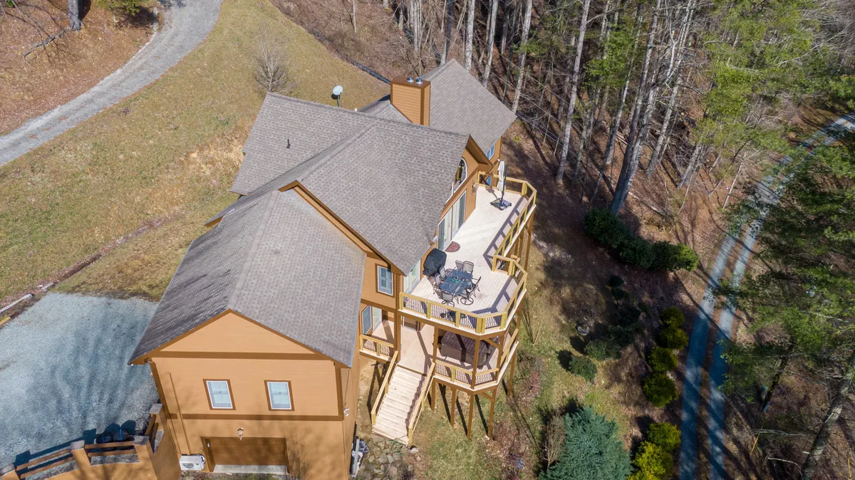 An expansive wooden deck bordered by mature trees and featuring the home's driveway. The scene showcases an inviting outdoor living space for dining or relaxing, with the driveway visible, hinting at easy gear access and winter vehicle requirements.