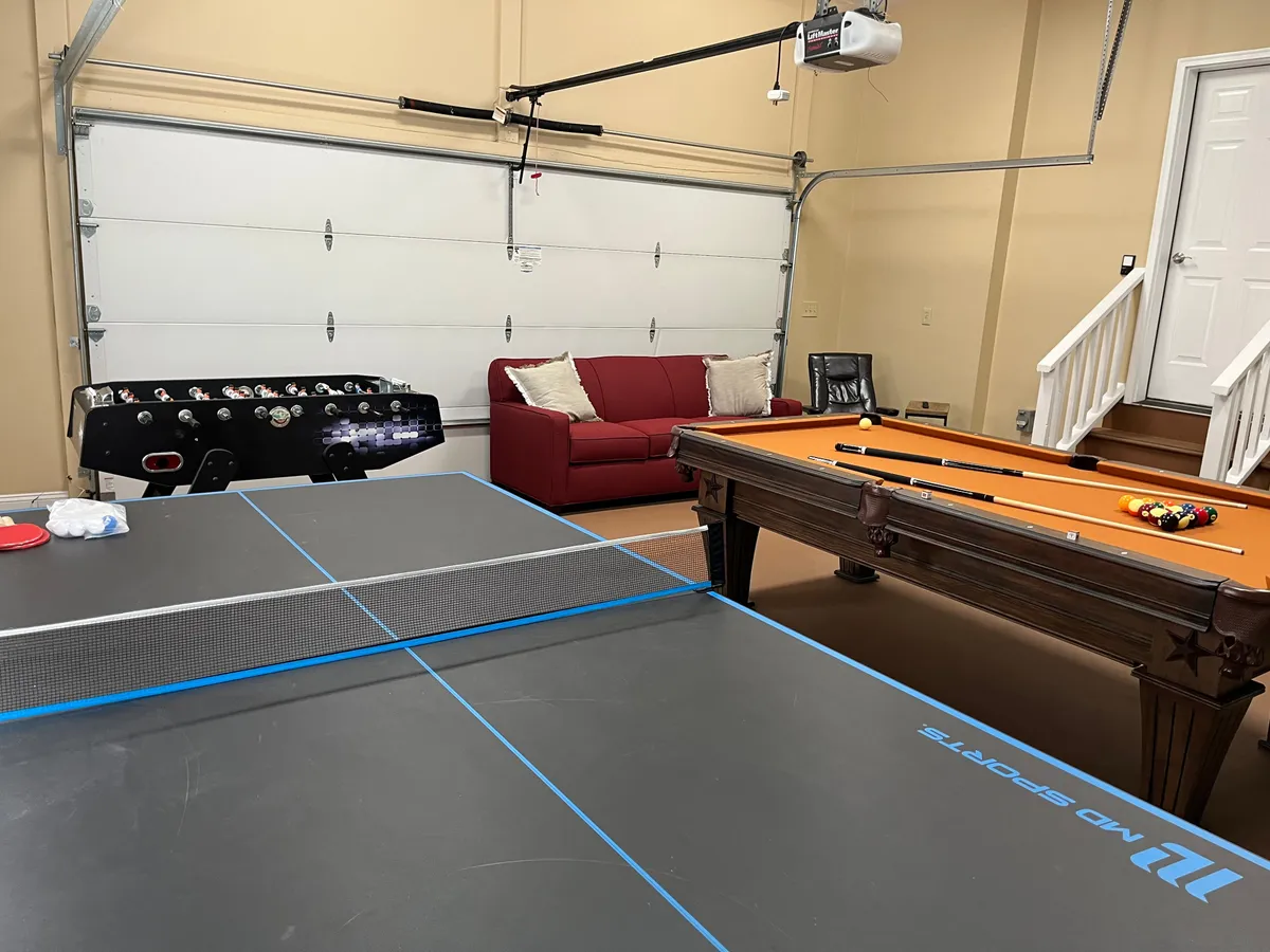 A vibrant game room featuring a ping pong table, pool table, and foosball table, with a red couch inviting relaxation. The space is clearly designed for fun and socializing, with ample room for group activities and comfortable seating. The overall vibe is energetic and casual, perfect for friendly competitions and game nights.
