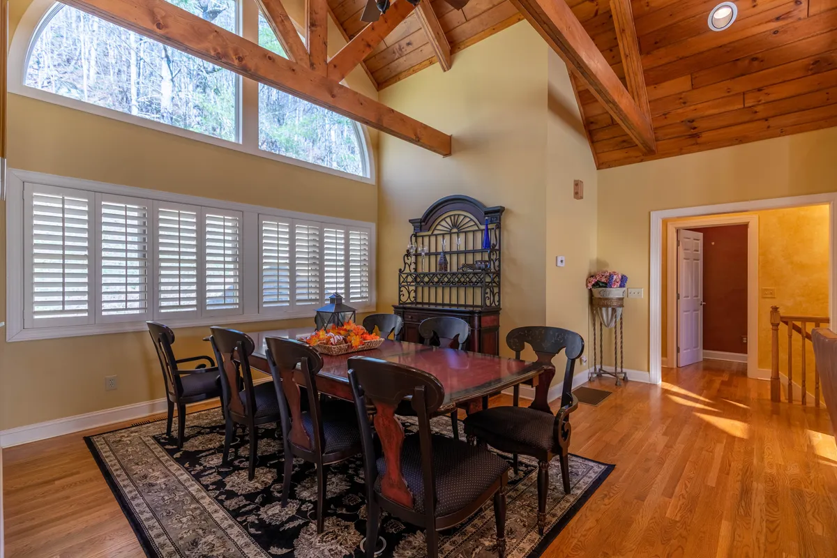 A large dining area with a substantial table comfortably seating eight, accented by exposed wooden beams and bathed in natural light from nearby windows. Decorative shelving and subtle details convey a festive yet welcoming setting for shared meals and celebrations.