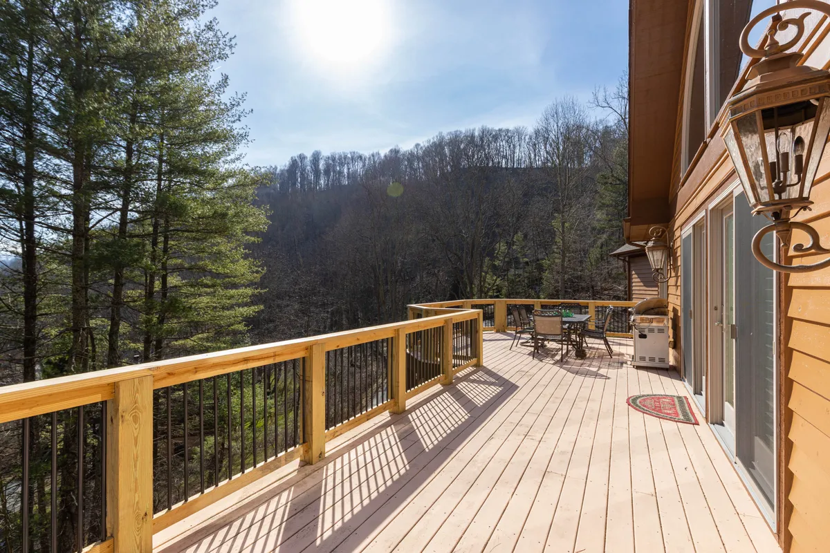 A spacious wooden deck bathed in sunlight, complete with a stylish dining set and a backdrop of lush greenery. The scene is serene and inviting, offering space for outdoor dining, morning coffee, and quiet evenings.