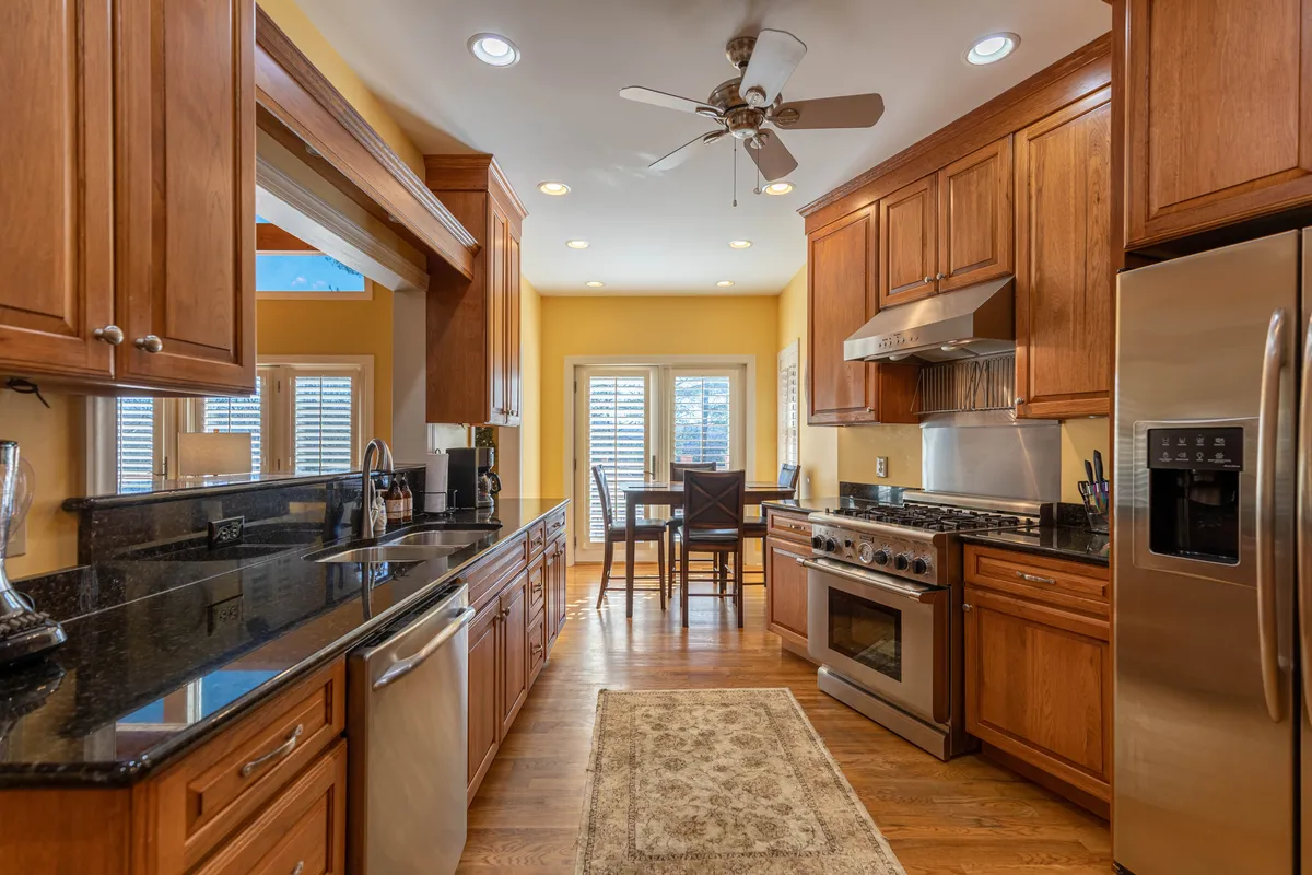 A warm, inviting kitchen scene featuring a central island, modern stainless steel appliances, and rich wooden cabinetry. The open design connects seamlessly with the adjacent dining area, suggesting effortless flow for entertaining and meal preparation.