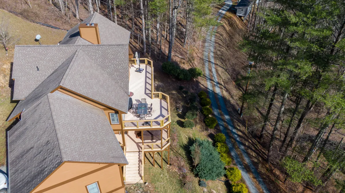 The image displays a spacious deck with ample seating, surrounded by tall trees and natural greenery. A walking path leads away from the deck, inviting exploration of the tranquil outdoor setting. The area is set up for both relaxation and social gatherings, with comfortable outdoor furniture and views that highlight the natural scenery.