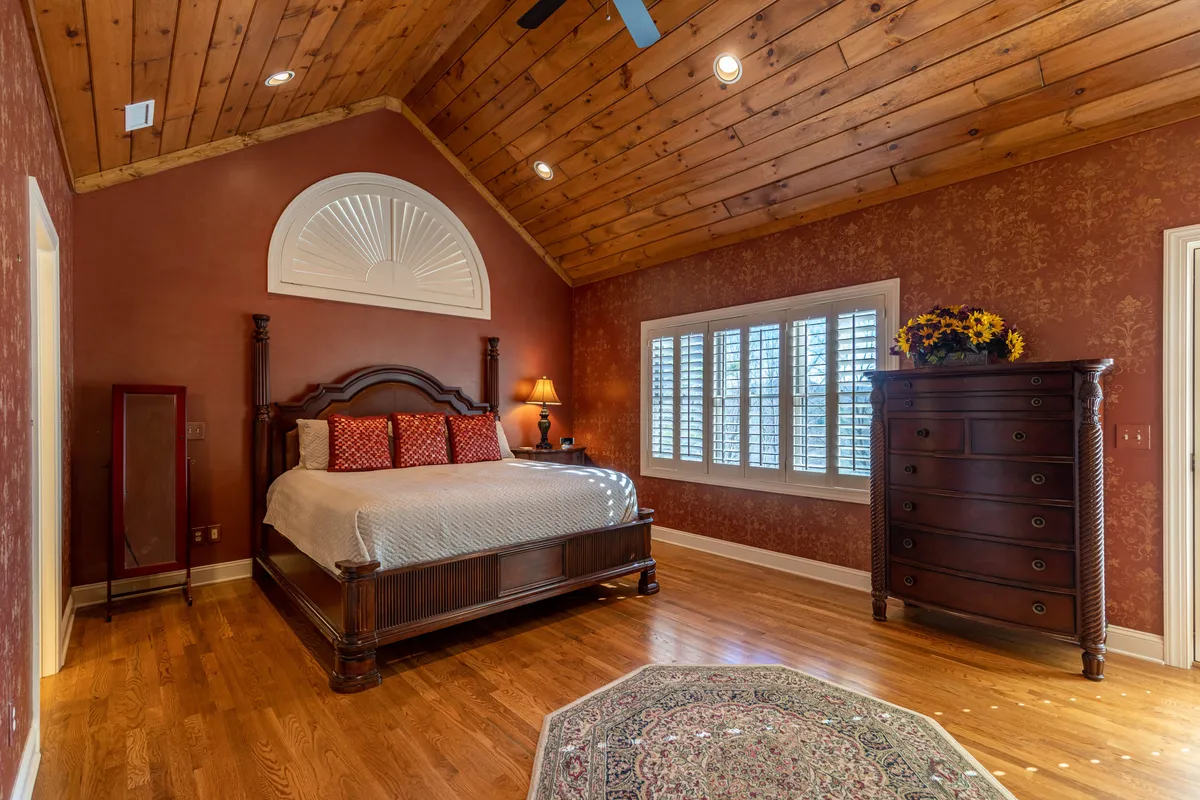 A cozy bedroom featuring a king bed dressed in plush linens, elegant dresser, and shuttered windows that allow soft morning light to fill the space. Decorative wall features and a comfortable reading nook contribute to the inviting, restful atmosphere.