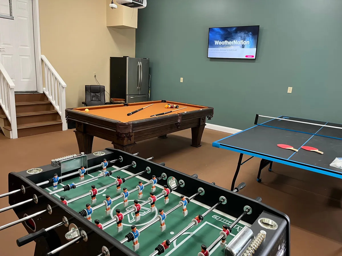A spacious recreation area equipped with a foosball table, pool table, ping pong table, and large television, providing various options for entertainment. The seating area ensures comfortable viewing and socializing, while the setup allows for simultaneous games and group fun.