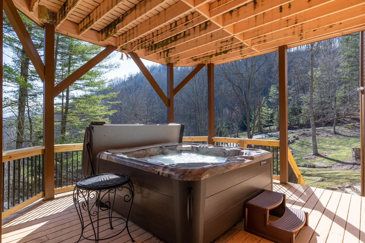 This exterior image features a bubbling hot tub on a spacious wooden deck, surrounded by lush green trees. The setting exudes tranquility and offers a seamless connection to nature, perfect for unwinding after adventurous outdoor activities.